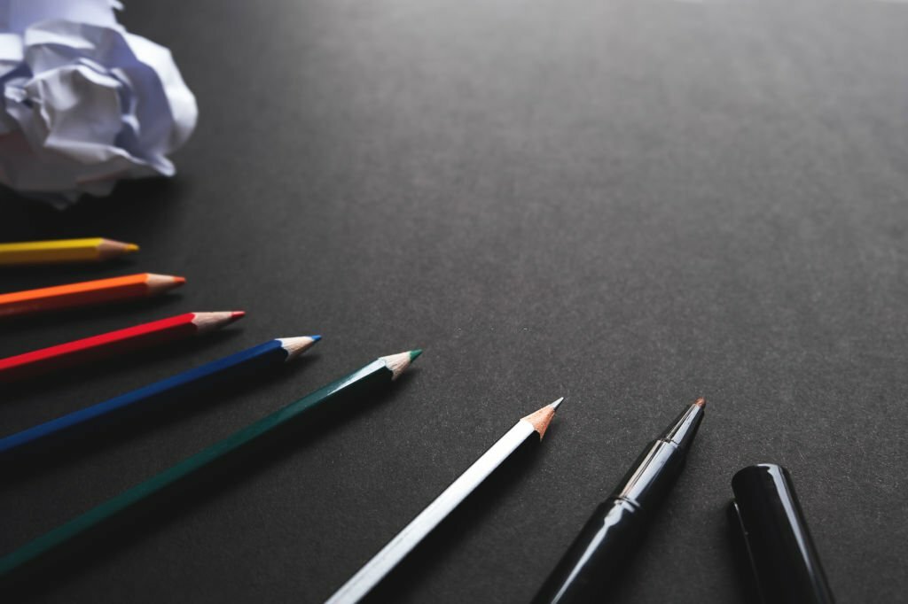 Top view of color pencil, pencil, black magic pen, crumpled paper and black background